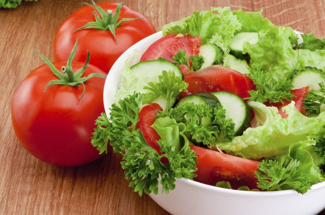 Bowl of mixed salad against and tomatoes is wooden table