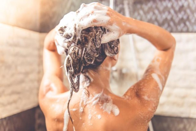 Back view of beautiful naked young woman is using shampoo while taking shower in bathroom