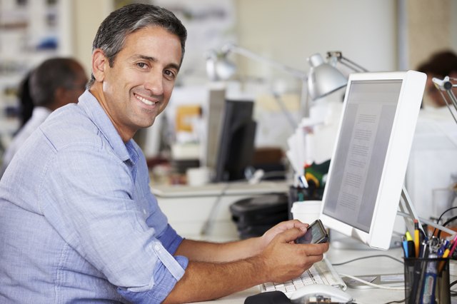 Man Using Mobile Phone At Desk In Busy Creative Office