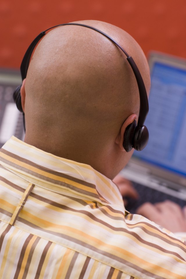 Rear view of a male customer service representative wearing a headset sitting in front of a laptop