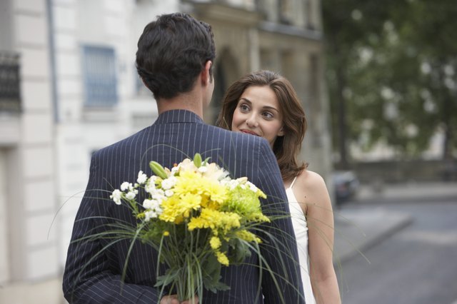 France, Paris, young couple outdoors, man holding flowers behind back