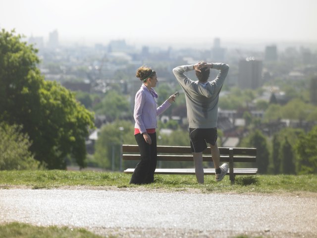 Man and woman resting after exercises, man stretching looking at cityscape, woman holding mobile phone