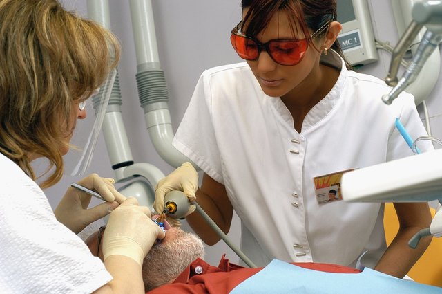 Female dentist and dental assistant working on male patient, close-up