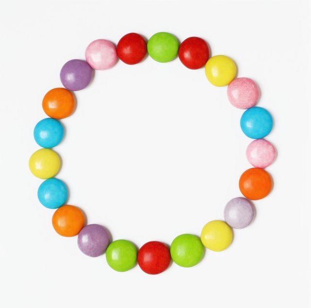 Multi-coloured candies arranged in form of circle on white background, overhead view