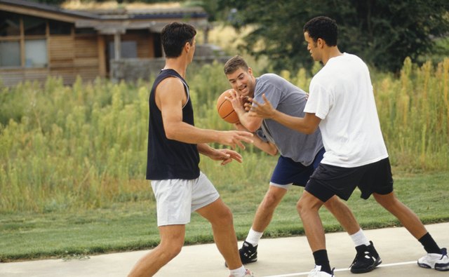 Three teenage boys (16-17) playing basketball on outdoor court