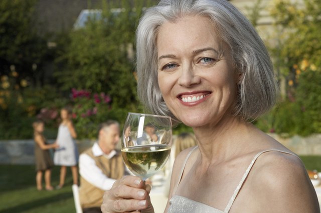 Mature woman in garden holding wine glass, smiling, portrait, close-up