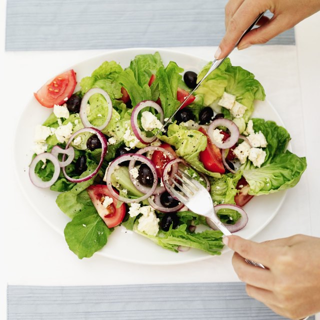 Person tossing salad with a fork and knife