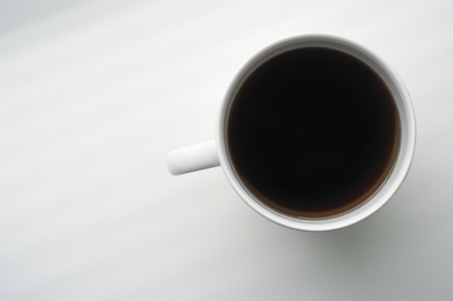 Overhead view of cup of black coffee on white surface