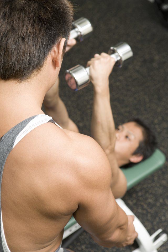 Men exercising in gym, one man lifting dumbbell, high angle view, differential focus