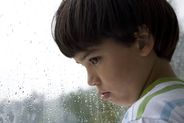 Boy (8-9) looking out window on rainy day