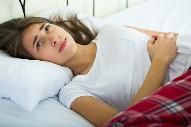 Portrait of brunette girl in bed with stomach pain