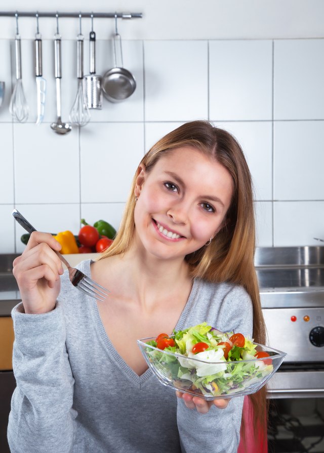 Laughing young woman at kitchen with fresh salad