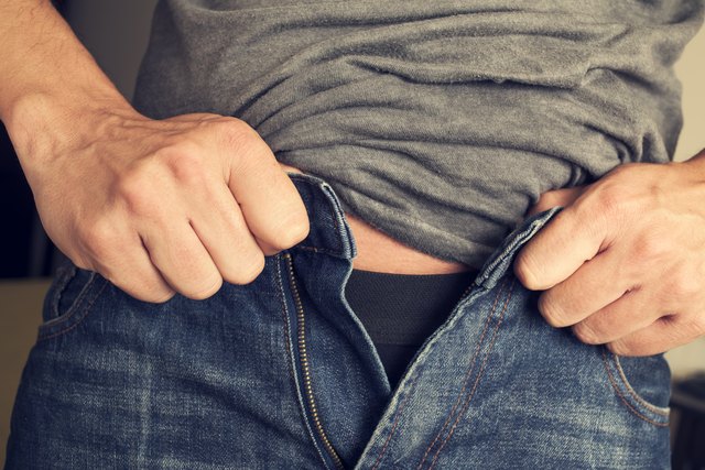 young man trying to fasten his trousers