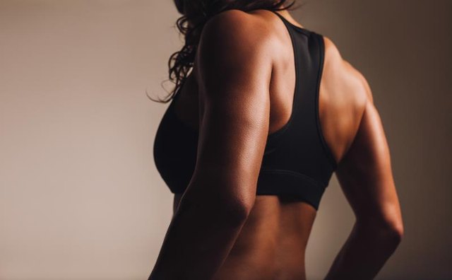 A fit, muscular woman in a sports bra shows off her lats.