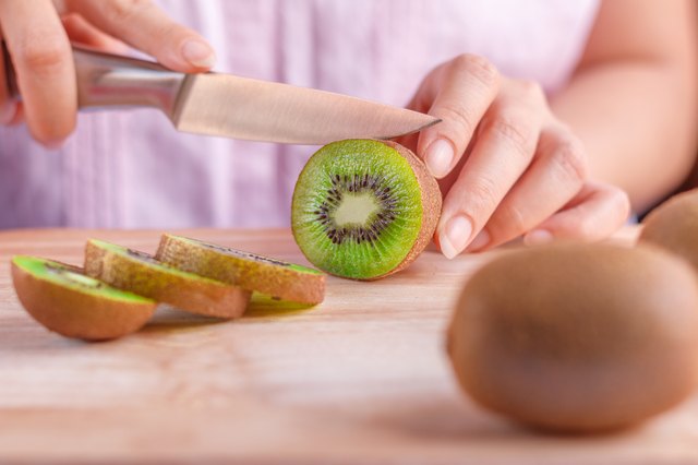 Woman food preparation - cutting a kiwi fruit.