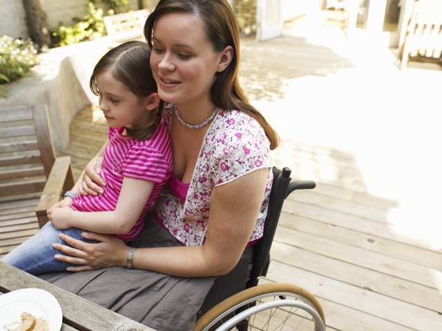 Woman sitting in wheelchair, with daughter (6-8) on lap, smiling