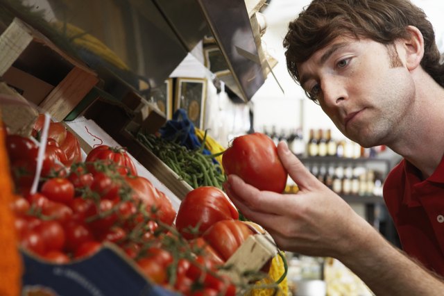 Young man in shop examining large tomato, close-up