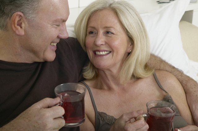 Mature couple holding cups of tea in bed, smiling, close-up