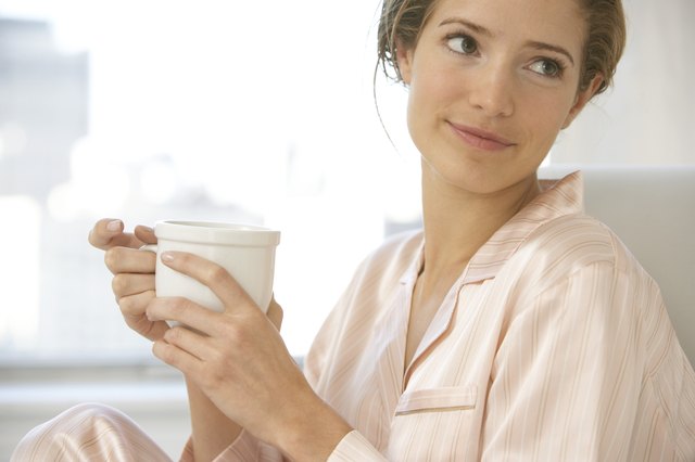 Young woman wearing pyjamas, holding cup, looking to side