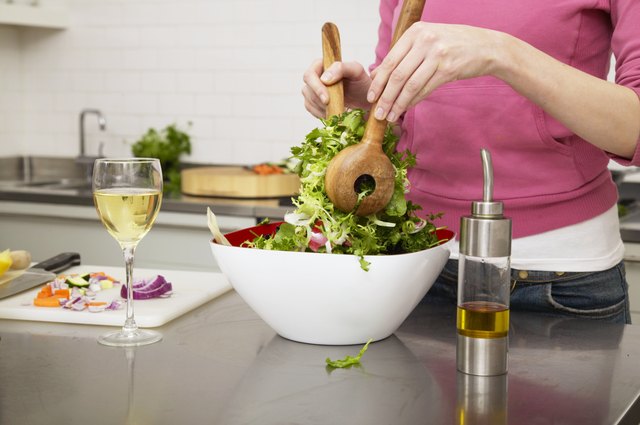 Young woman preparing salad in kitchen, mid section