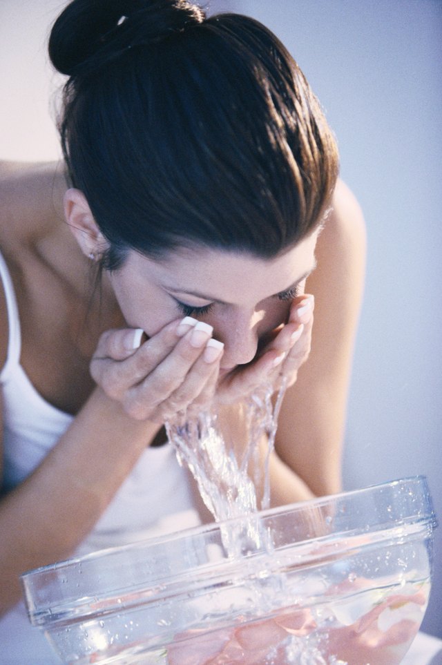 Young woman washing her face in a bowl of water