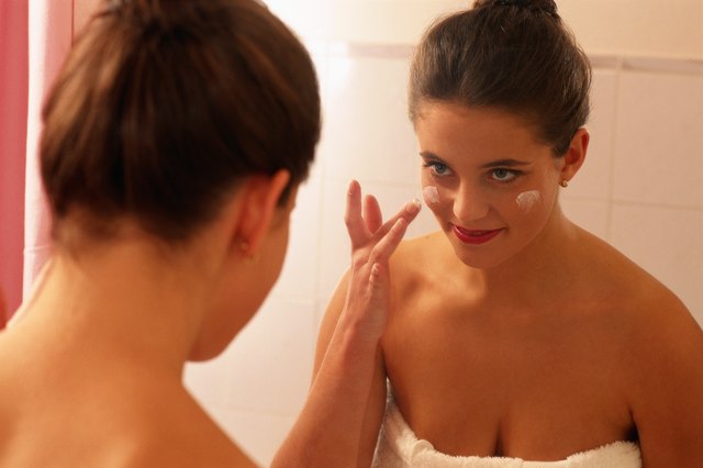 Woman standing in front of mirror, applying face cream