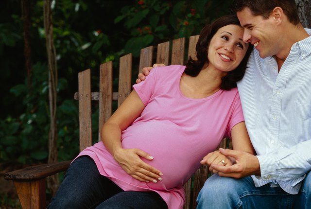 portrait of a couple expecting a baby sitting on a park bench