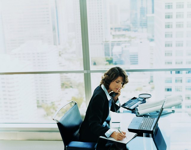 Businesswoman Sitting at Her Desk Using the Phone and Writing in a Notepad