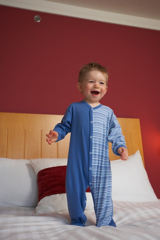 Smiling toddler boy standing atop hotel bed