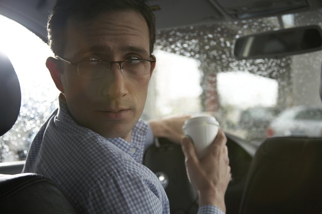 Man drinking coffee while driving car, looking over shoulder