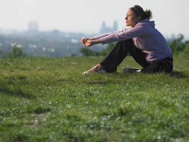Young woman sitting on grass in sport clothes, cityscape in background
