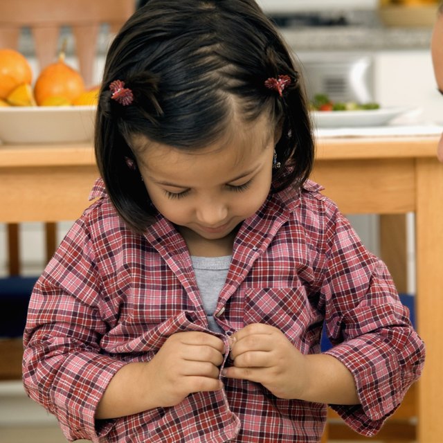 Young girl trying to button her shirt