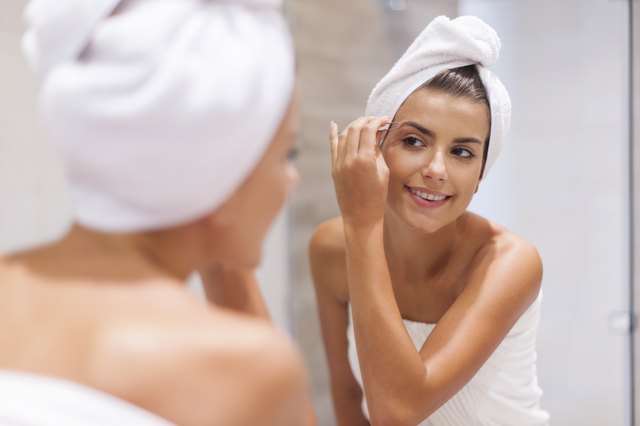 Happy young woman tweezing eyebrows