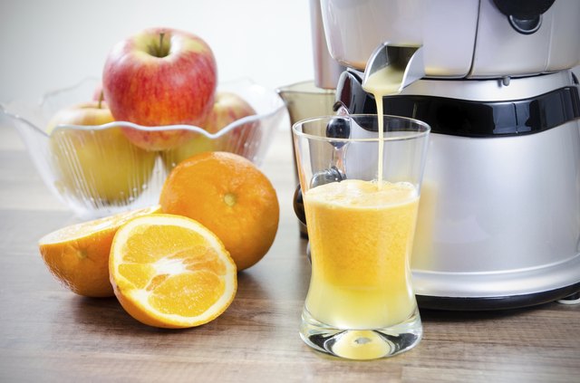 Juicer and orange juice. Fruits in background