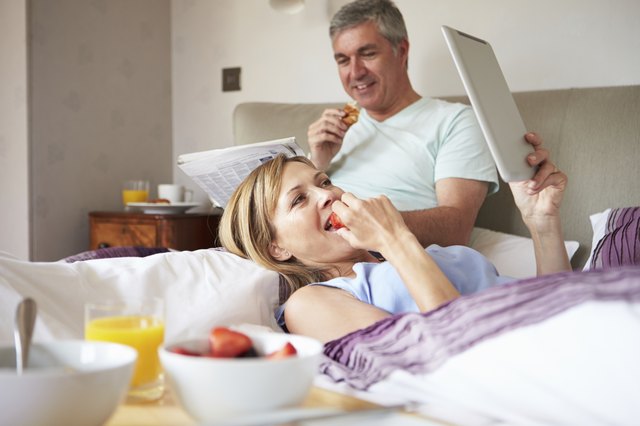 Couple Eating Breakfast In Bed With Paper And Digital Tablet