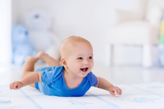 Adorable baby boy in white sunny bedroom. Newborn child relaxing on a rug. Nursery for young children. Furniture, textile and bedding for kids. New born kid during tummy time with toys at a window.