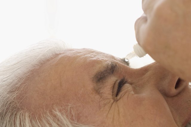 Smiling mature man applying eye drops into eye, extreme close-up