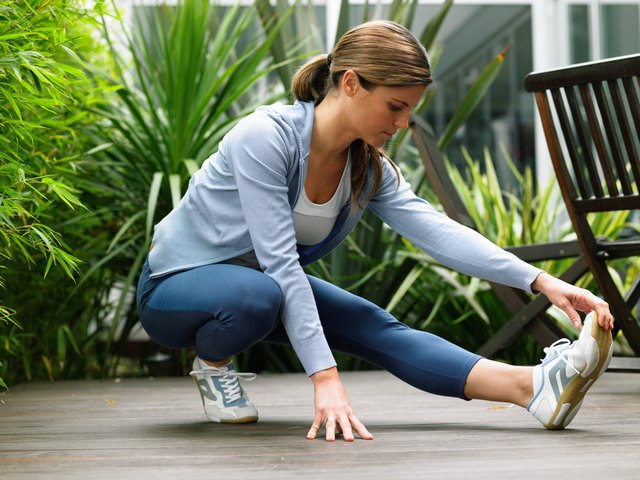 Woman wearing running clothes performing leg stretch in garden
