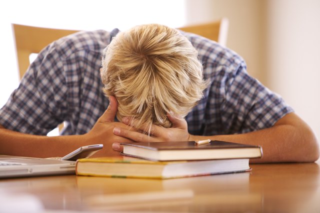 A boy lies his head down on the table while doing homework