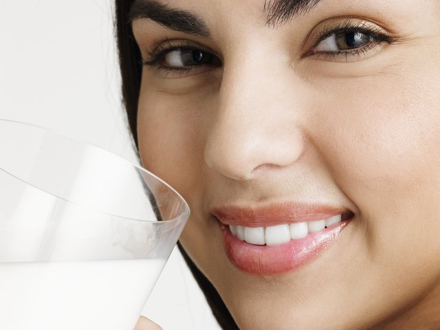 Young woman holding glass of milk, smiling, portrait, close-up of face