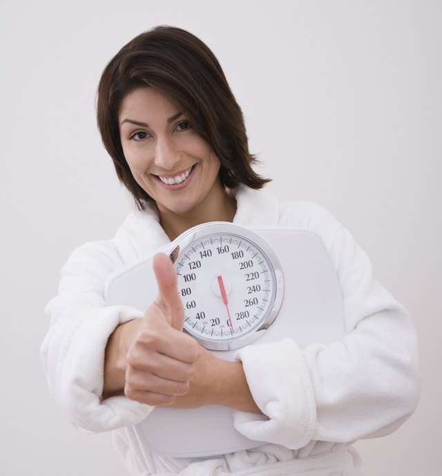 Hispanic woman holding scale and giving thumbs up