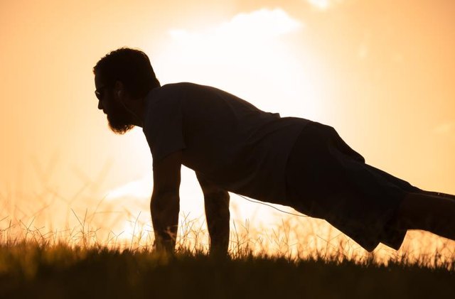 Silhouette of male doing push ups in the park.