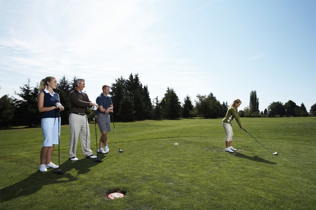 Group of golfers watching female golfer tee off
