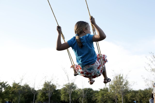 Young girl (8-9) swinging outdoors, rear view