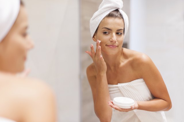 Gorgeous woman applying moisturizer on face