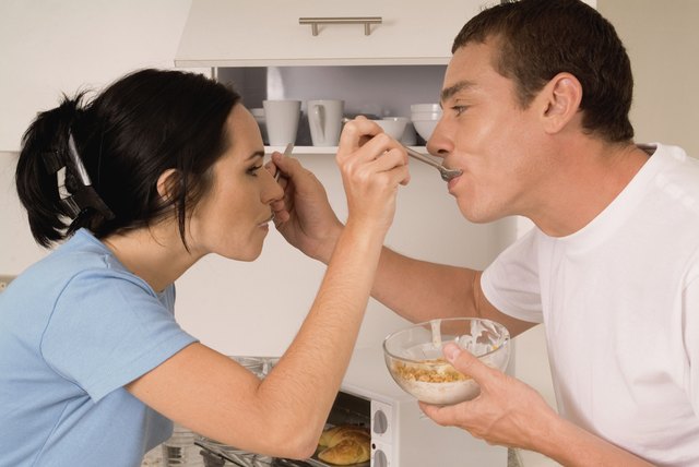 Couple feeding each other cereal in kitchen, close-up