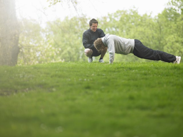 Two men in park, one doing push-ups other squatting and watching