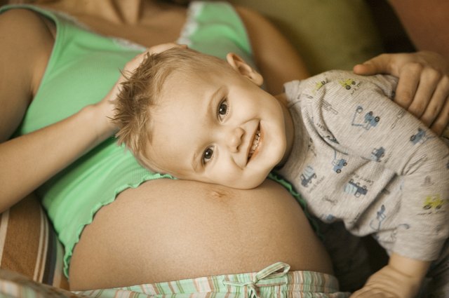 Pregnant mother lying in sitting room, cuddling young son to stomach, close-up