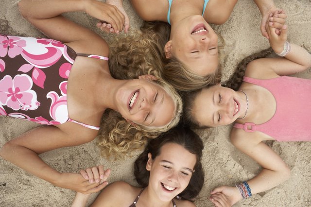 Four girls (8-12) lying in circle on beach, holding hands, eyes closed