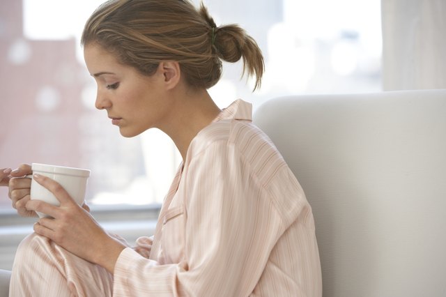 Young woman on sofa, looking at cup, close-up, profile